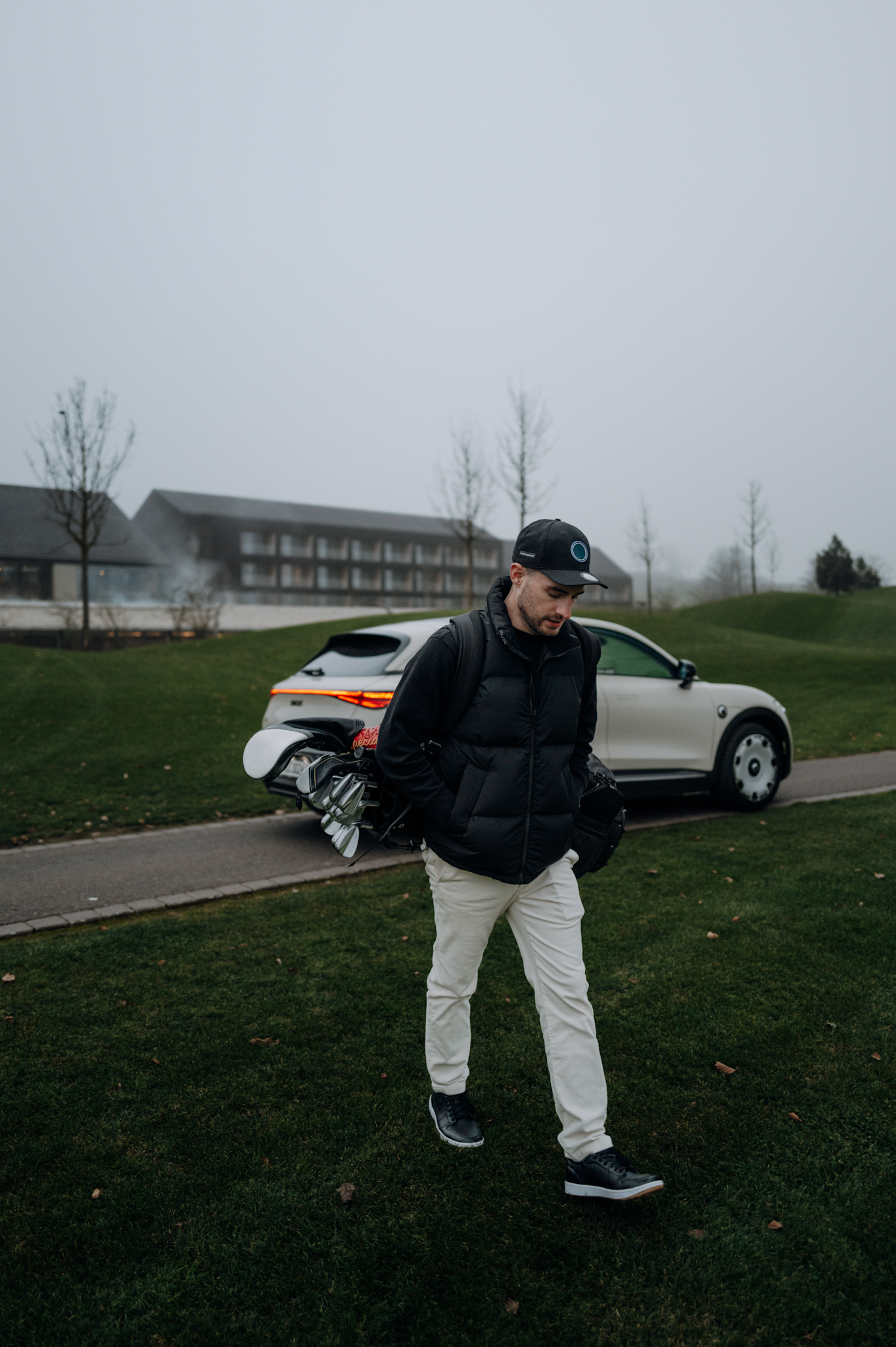 Man walking across a golf course with a golf bag, Smart #3 Premium in the background.